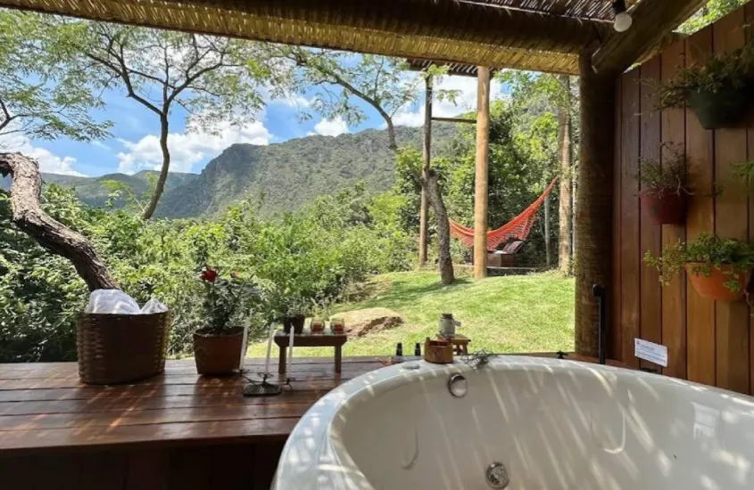 Banheira de hidromassagem ao ar livre com vista para as montanhas verdes em uma cabana charmosa em Casa Branca, um lugar onde se hospedar para conhecer Inhotim