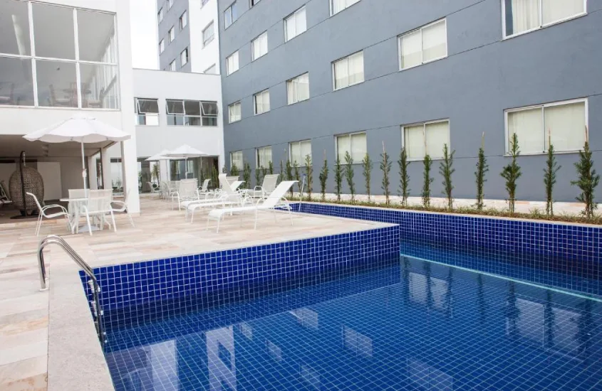 Piscina moderna em área externa do Hotel Abba Uno, em Contagem, com cadeiras confortáveis e ambiente tranquilo para um dia de descanso ao sol