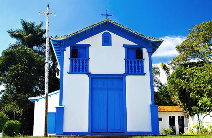 Pequena igreja com detalhes em azul e branco, iluminada pelo sol do meio-dia, em São Sebastião das Águas Claras, popularmente conhecido como Macacos, um vilarejo pitoresco e acolhedor perto de Belo Horizonte