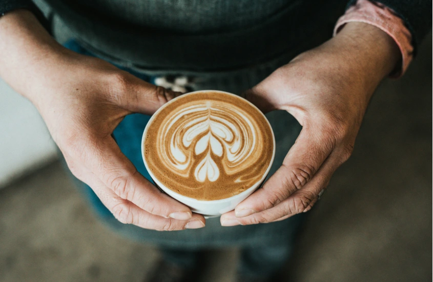 Mãos segurando um cappuccino com latte art em uma cafeteria, um dos destaques da cultura australiana