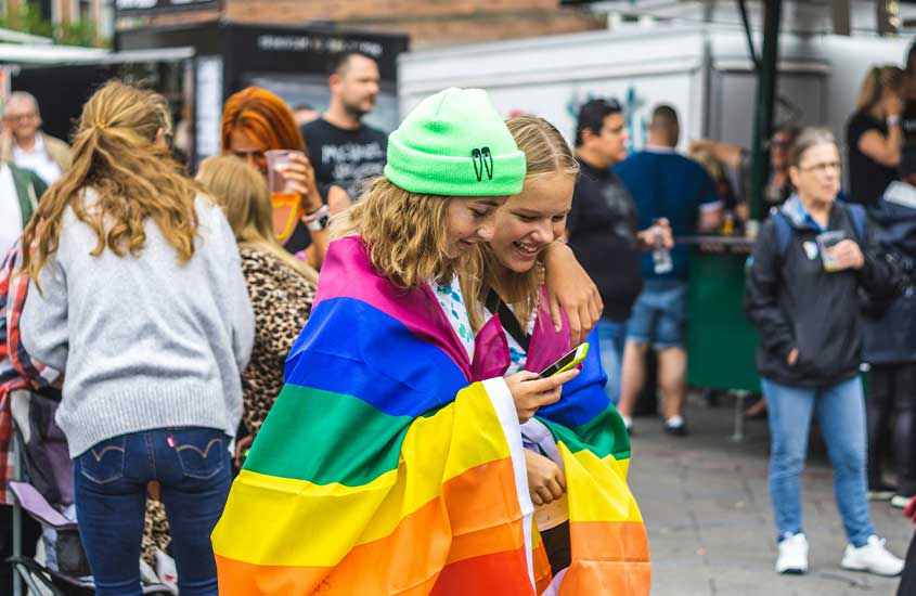 Duas jovens envoltas em uma bandeira do orgulho LGBTQIA+ durante um evento de rua na Dinamarca