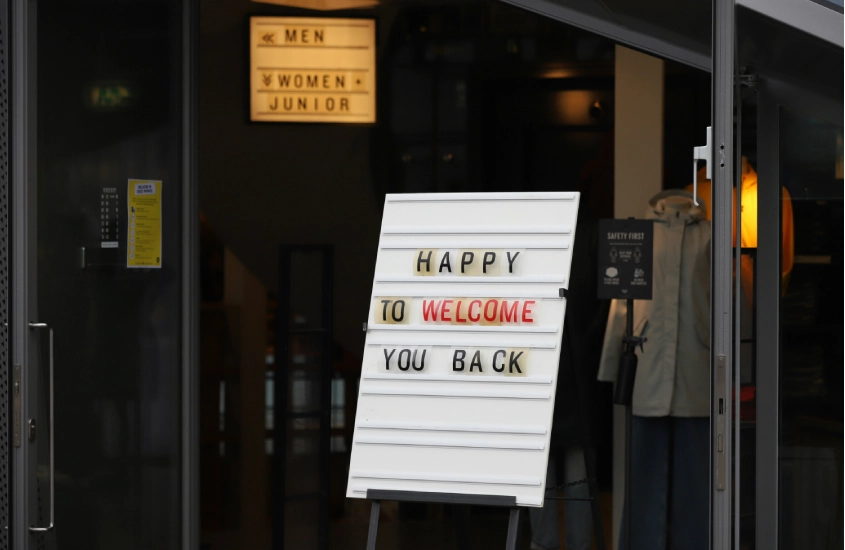 Placa em frente a uma loja com os dizeres "Happy to welcome you back" (Felizes por recebê-lo de volta), em um ambiente urbano