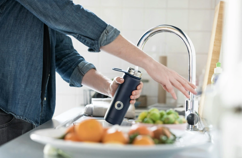 Uma pessoa enchendo uma garrafa reutilizável de água em uma pia de cozinha