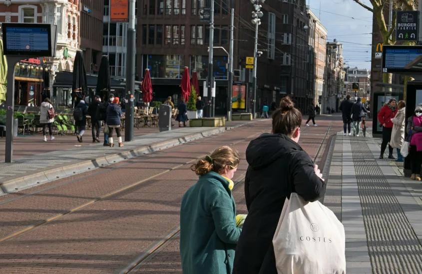 Pessoas caminhando em uma rua de Amsterdam com trilhos de bonde ao fundo