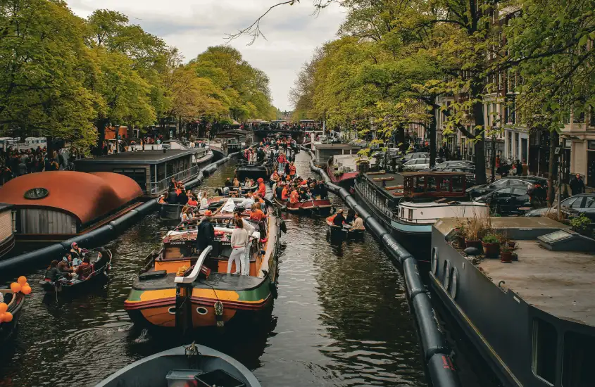 Barcos cheios de pessoas navegando por um canal em Amsterdam durante uma celebração