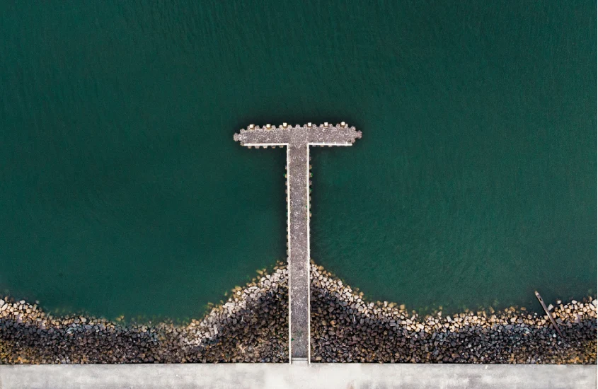 Vista aérea de um pier em formato de “T” rodeado por pedras e águas calmas