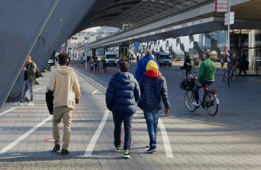 Pessoas caminhando e ciclistas circulando sob uma ponte moderna em uma área urbana