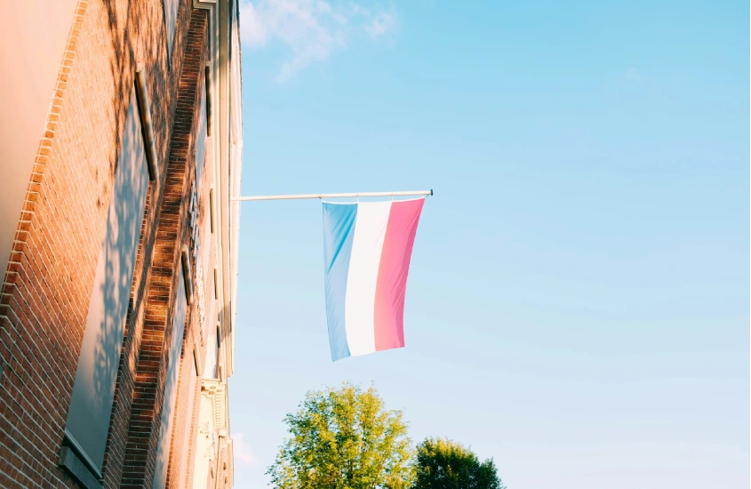 Bandeira da Holanda pendurada em uma fachada de tijolos sob o céu claro e azul