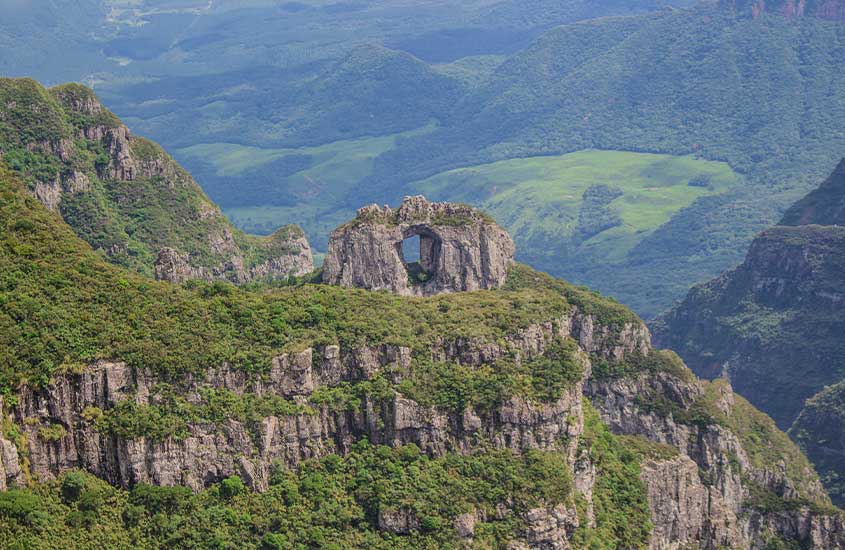 Formação rochosa conhecida como Pedra Furada em Urubici, com montanhas verdes ao fundo