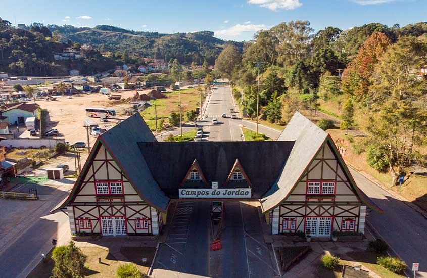 Estrutura arquitetônica em estilo alpino marcando a entrada da cidade de Campos do Jordão, cercada por montanhas verdes ao fundo