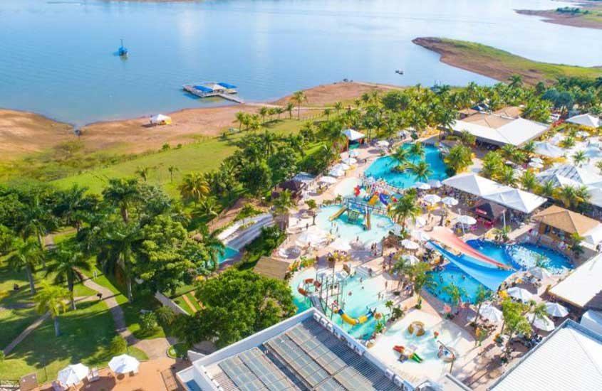 Vista aérea de um complexo aquático com várias piscinas e áreas de lazer ao lado de uma lagoa