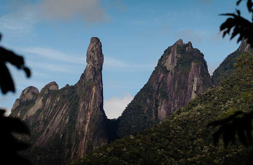 Montanha icônica Dedo de Deus com picos afiados cercados por vegetação verde. O céu azul completa o visual da natureza