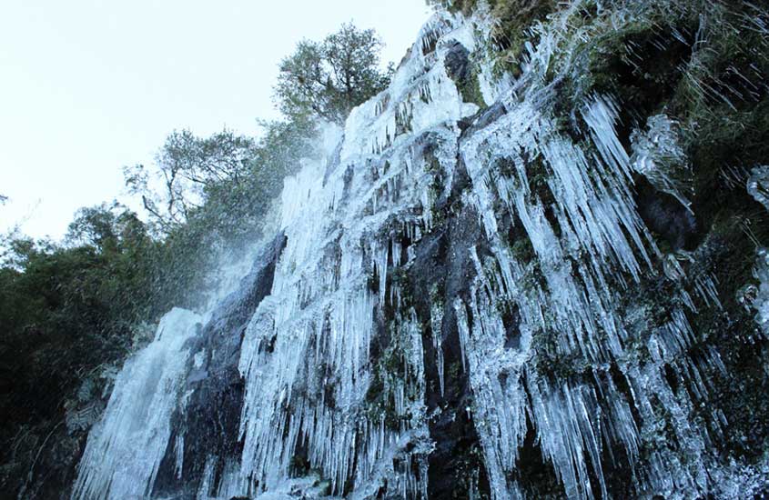 Cachoeira completamente congelada em Urupema, com formações de gelo pendentes das rochas e vegetação ao redor