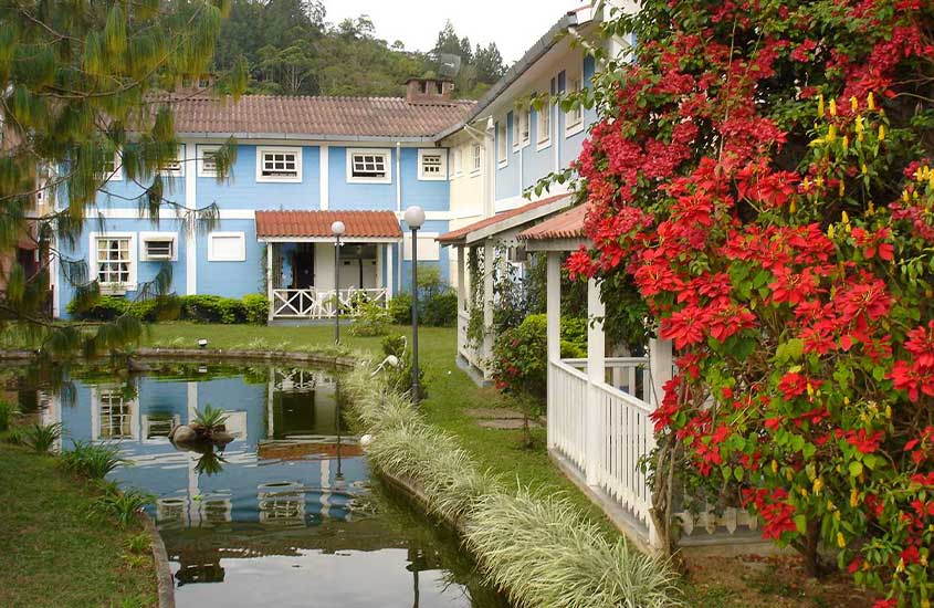 Casas de arquitetura colonial cercadas por flores e vegetação ao lado de um pequeno lago em Penedo