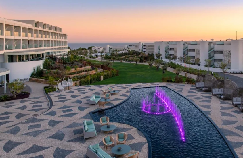 Piscina moderna com fontes iluminadas e área de lazer ao pôr do sol no W Algarve