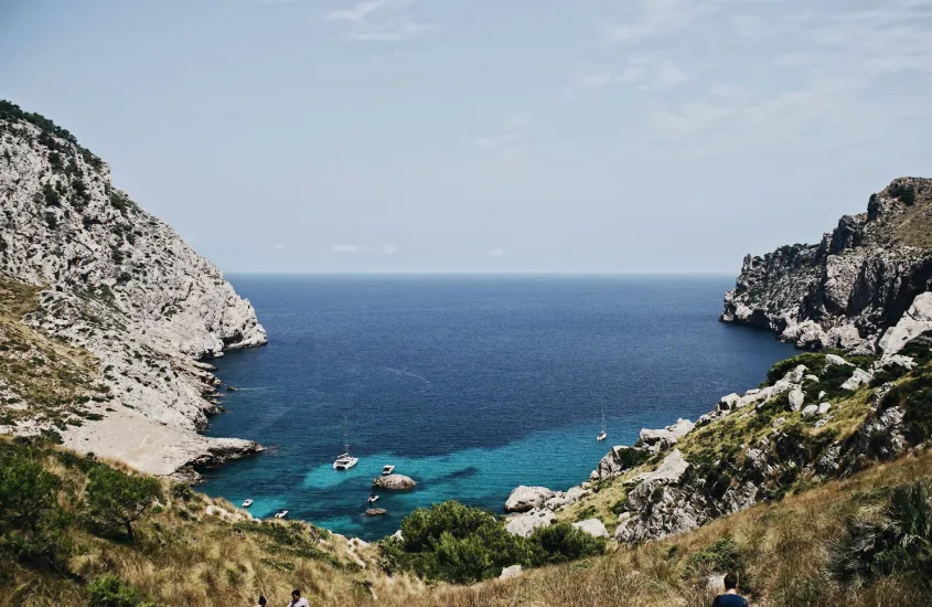 Enseada rochosa cercada por colinas em Cala Figuera, Maiorca, com águas azuis profundas e barcos flutuando calmamente