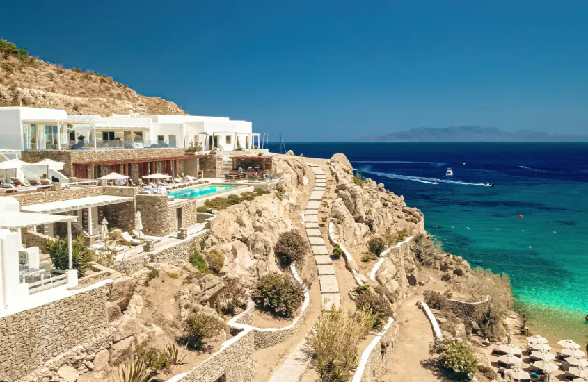 Casas brancas luxuosas com piscinas à beira de uma falésia, de frente para o mar azul profundo em Mykonos, sob um céu claro