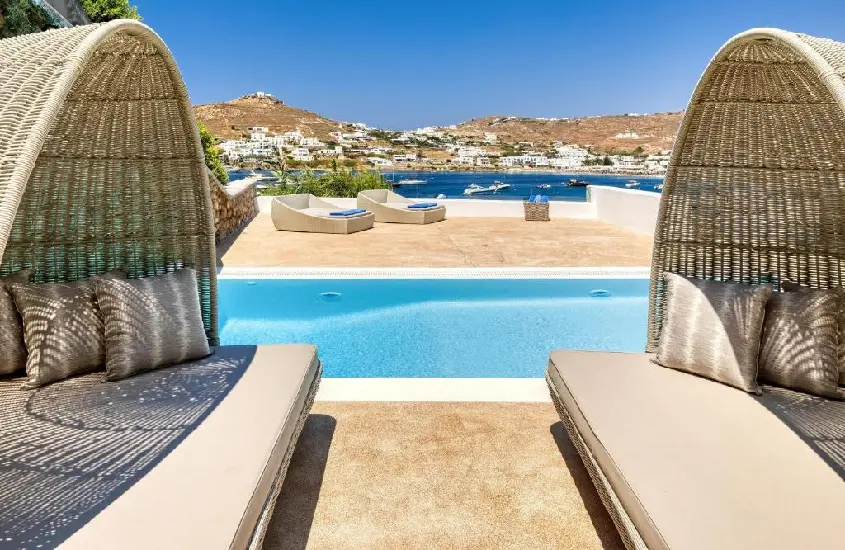 Camas de piscina com vista para o mar azul em Mykonos, cercadas por colinas sob um céu limpo e ensolarado