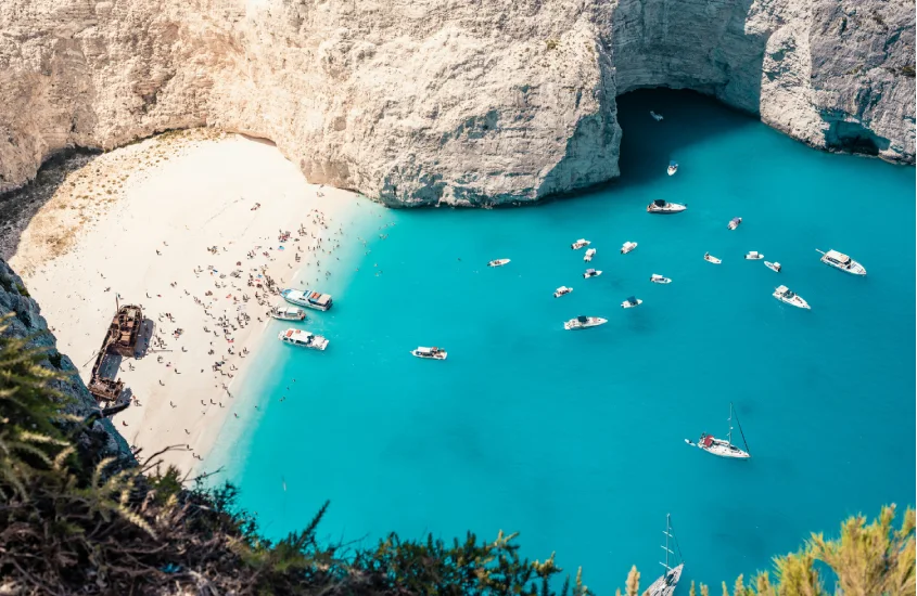 Praia isolada de Navagio, com águas cristalinas e falésias douradas, repleta de pequenos barcos aproveitando o dia ensolarado