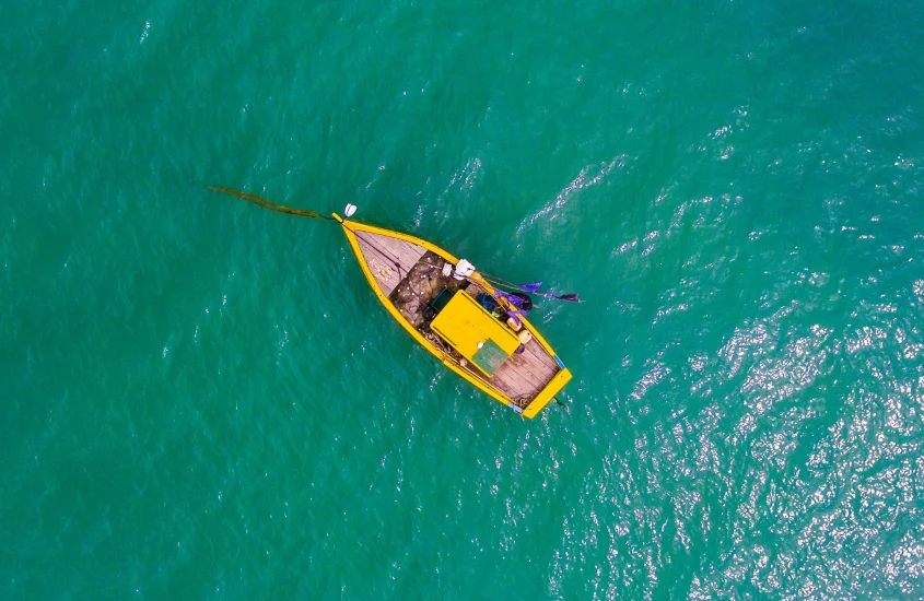 Vista aérea de um barco de pesca solitário em águas cristalinas e esverdeadas ao meio-dia na Praia do Espelho, um dos melhores destinos para relaxar no Brasil