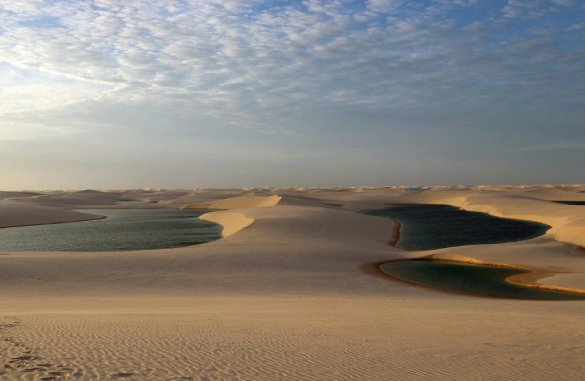 Dunas douradas dos Lençóis Maranhenses ao entardecer, com lagoas esverdeadas refletindo a luz suave do sol