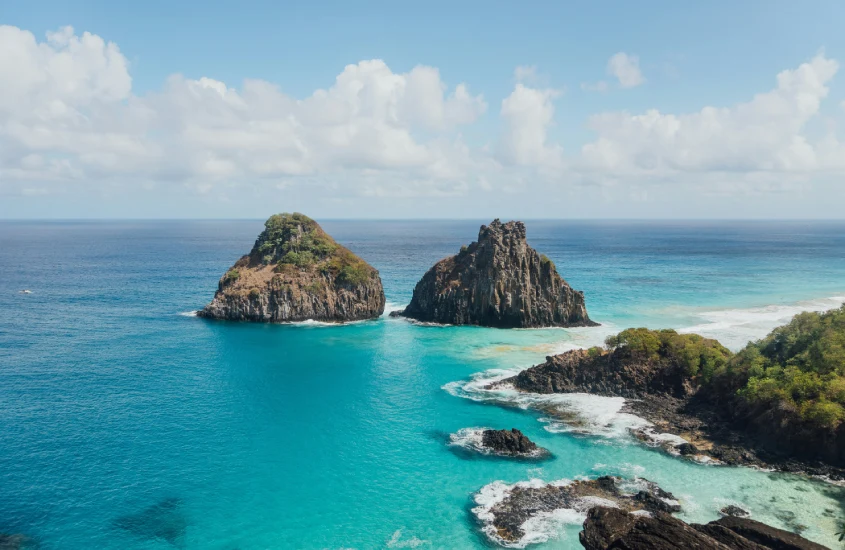 Formações rochosas icônicas de Fernando de Noronha em um dia ensolarado, com o mar azul-turquesa ao redor