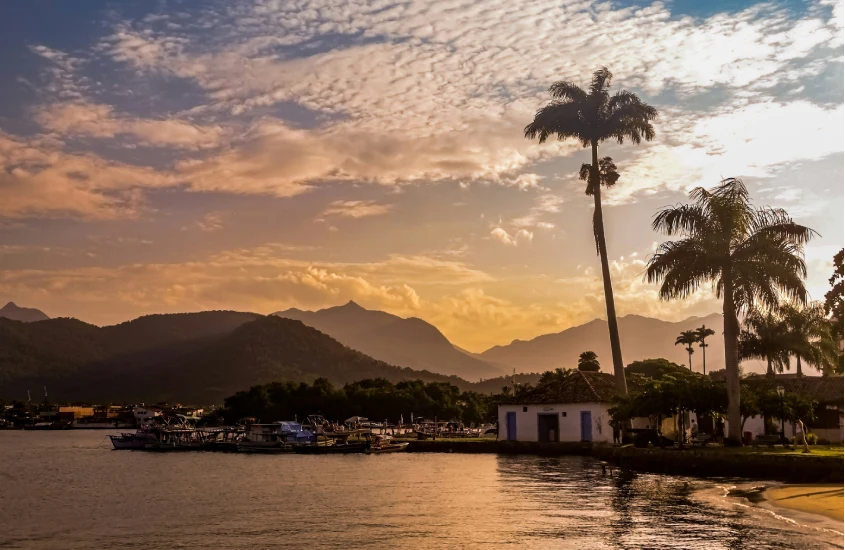 O pôr do sol em Paraty, com montanhas ao fundo e barcos atracados à beira-mar