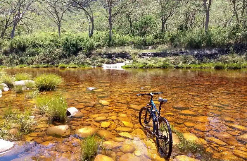 Bicicleta descansando em um riacho cristalino em Serra do Cipó, capturada ao meio-dia, com árvores e vegetação densa ao fundo