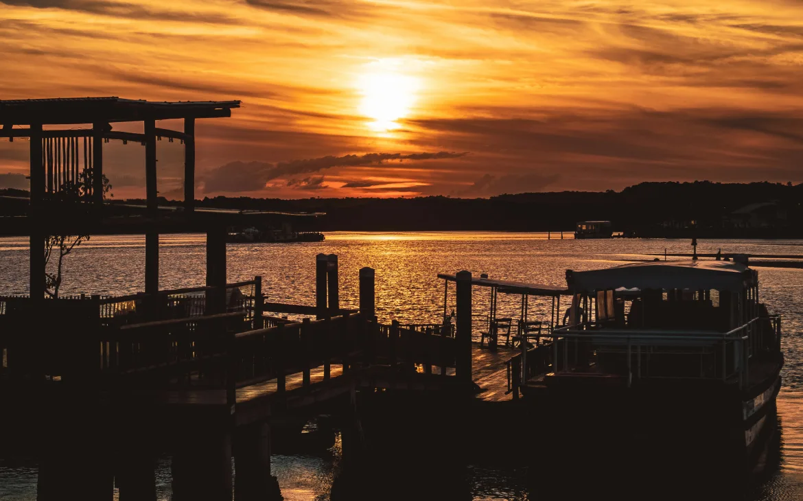 Pôr do sol deslumbrante refletido nas águas tranquilas, com um barco ancorado e uma estrutura de madeira compondo o cenário de um dos melhores destinos para relaxar no Brasil