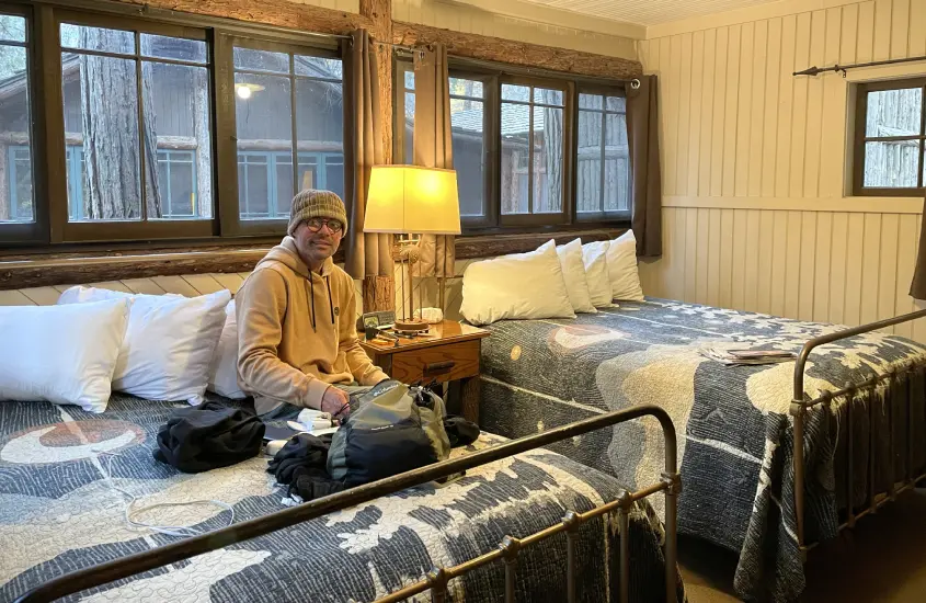 Vagner Alcantelado sentado em uma cama de madeira em um quarto rústico de um dos hotéis onde ficar em Yosemite