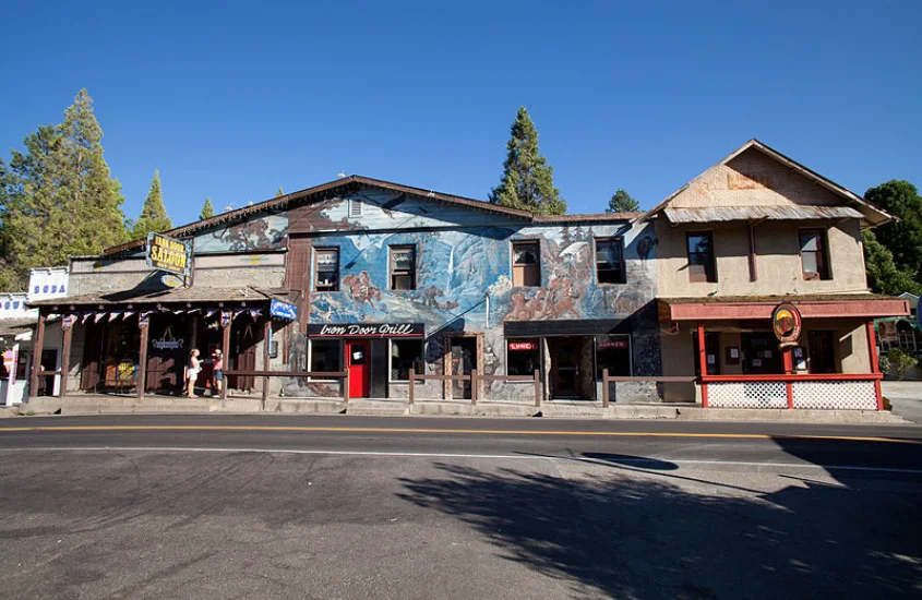 Um edifício histórico com pintura mural nas paredes externas, localizado na cidade de Groveland, Califórnia. A fachada tem cores desgastadas e exibe o "Iron Door Saloon", um famoso bar local com um estilo rústico