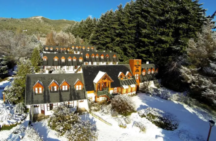 Fachada do Rupu Pehuen Resort coberta por neve e rodeada por florestas, criando um cenário ideal para curtir o inverno na Patagônia Argentina