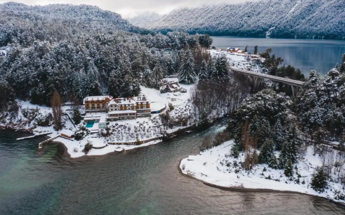 Durante o dia, vista aérea do Correntoso Lake & River Hotel cercado por florestas cobertas de neve, às margens de um lago