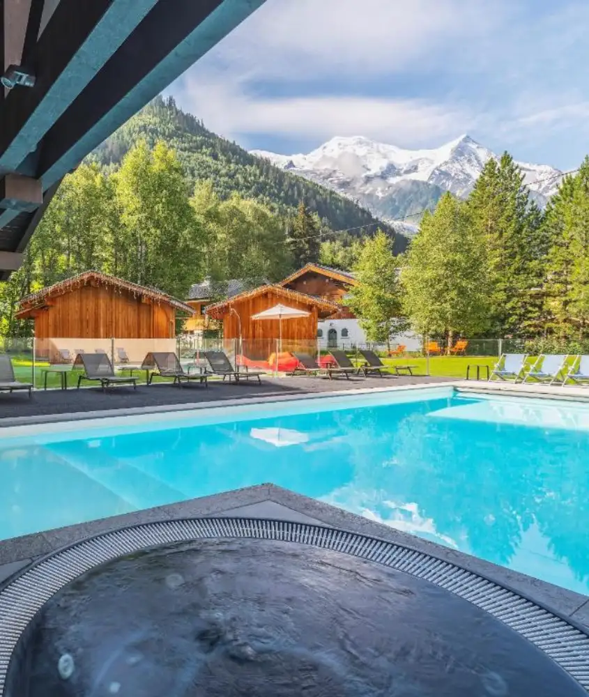 Piscina ao ar livre com vista para as montanhas nevadas, cercada por cabanas de madeira no Hôtel Le Refuge des Aiglons, um dos melhores resorts de inverno na França