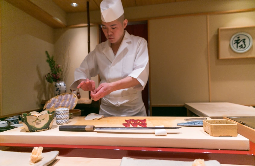 Um chef de sushi preparando delicadamente um prato em um restaurante tradicional de sushi em Ginza, com utensílios e ingredientes à sua disposição