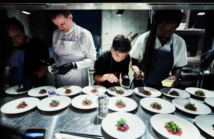 Um grupo de chefs trabalhando em conjunto, decorando pratos com Wagyu em um restaurante de alta gastronomia no Japão, focados na apresentação dos alimentos