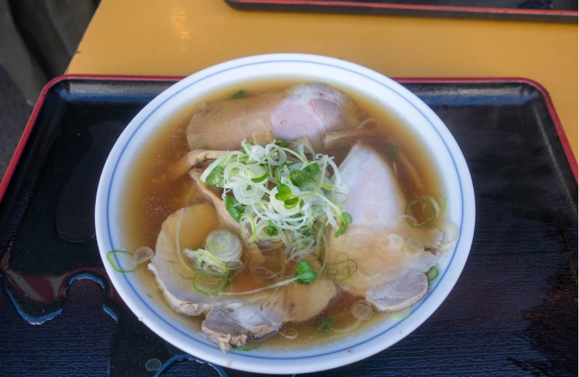 Tigela de ramen tradicional com fatias de carne de porco, cebolinha e caldo claro, servida em um prato branco