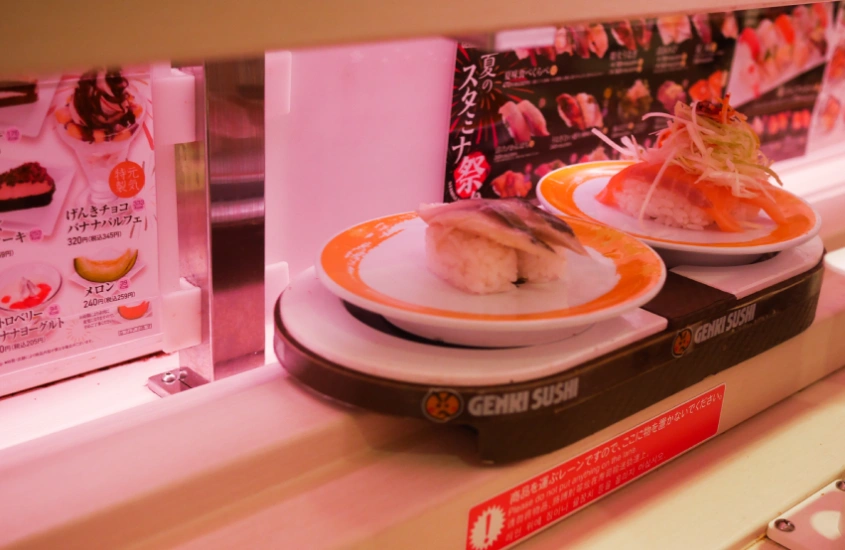 Pratos de sushi prontos para serem servidos no estilo kaiten sushi (esteira rolante), com duas porções em pequenos pratos coloridos passando em frente ao cliente