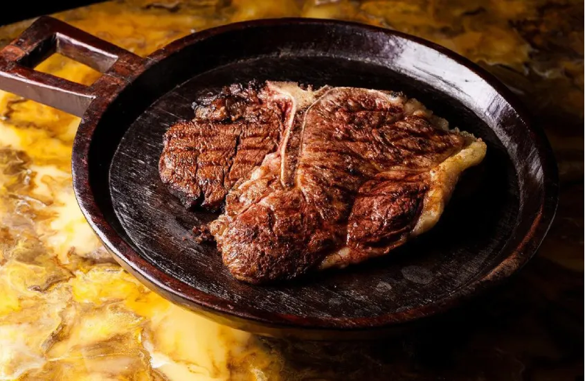 Um bife suculento servido em uma chapa de ferro sobre uma mesa de pedra com tonalidade amarela