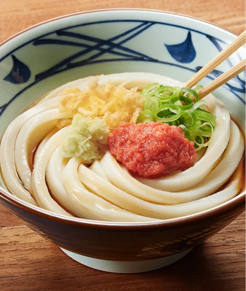 Um prato de udon japonês, com macarrão grosso coberto por gengibre ralado, cebolinha e uma pasta de peixe vermelho