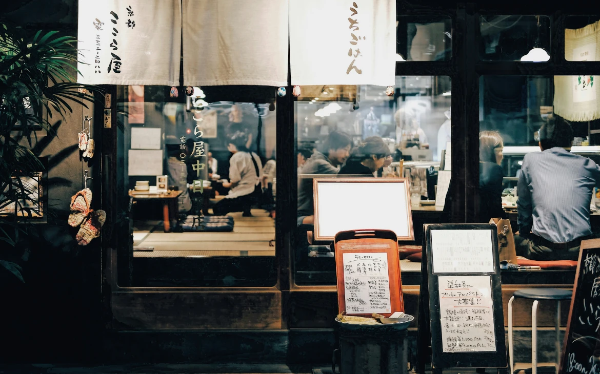 Fachada de um restaurante japonês tradicional com uma cortina branca na entrada, onde clientes podem ser vistos dentro, desfrutando de uma refeição