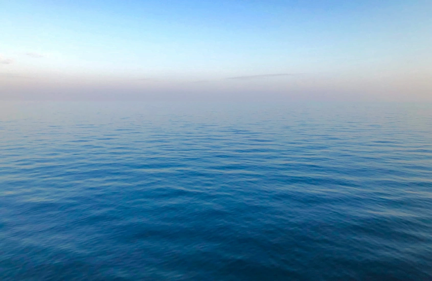 Um horizonte infinito de água calma e cristalina se funde com o céu, criando uma sensação de tranquilidade e vastidão.