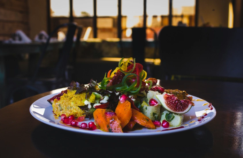 Um prato colorido e vibrante de comida gourmet, com uma variedade de vegetais, frutas e molhos em destaque, iluminado pela luz suave de um ambiente interior.