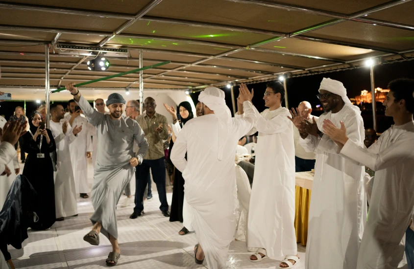 Homens vestindo trajes tradicionais árabes dançando em círculo, celebrando em um evento noturno.