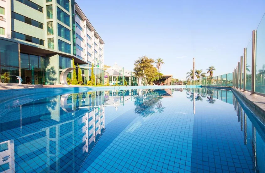 Piscina externa refletindo o céu azul em um resort com grande área ao ar livre, durante o dia