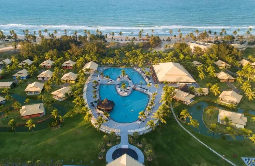 Resort de luxo à beira-mar com chalés e piscina em formato de lagoa, em uma área rodeada por palmeiras, durante o dia