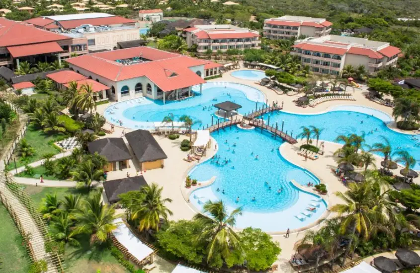 Vista aérea das grandes piscinas do Grand Palladium Imbassaí Resort & Spa, cercadas por áreas verdes e coqueiros.