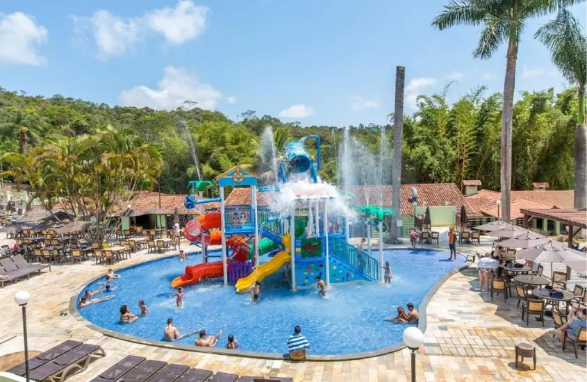 Piscina com brinquedos aquáticos no Tauá Hotel & Convention Caeté, cercada por área verde e cadeiras de sol.