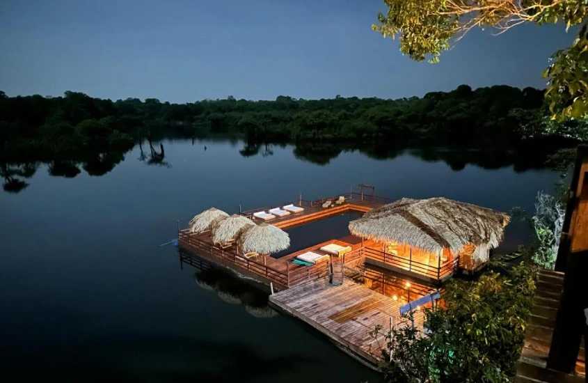 Um flutuante iluminado à noite, cercado por água calma e vegetação amazônica ao fundo.