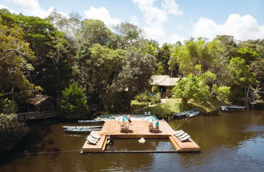 Um flutuante em meio à natureza amazônica, com pequenas embarcações ao redor e uma plataforma de descanso sob o céu claro.